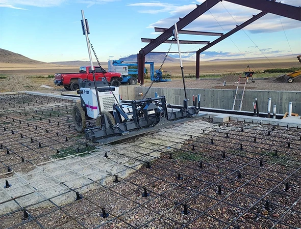 Concrete screed machine leveling a new foundation with rebar and gravel on a construction site.